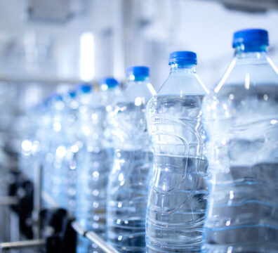 Close up view on plastic bottles of water in bottling factory being transported by conveyor belt automated machine.