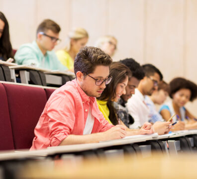 education, high school, university, learning and people concept - group of international students with notebooks writing in lecture hall